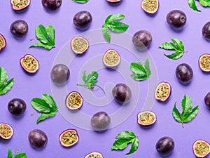 Pattern of dark purple passion fruits, it's halves and leaves on light purple table