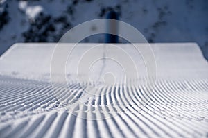 Pattern of a freshly groomed ski slope with one trace and a rail in the background