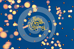 Pattern with golden Merry Christmas wording and holiday round sprinkles on classic blue with festive warm bokeh