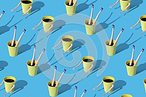 Pattern made of coffee cups with female doll hands and legs on blue background