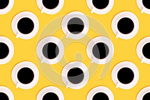 Pattern made of cup with black coffee on a yellow background.