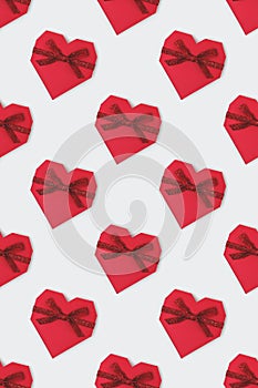 Pattern made of red gift box in a heart shape with tied glittering ribbon.