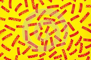 Pattern made from the red pieces of ribbons, isolated on a yellow background. View from the top.