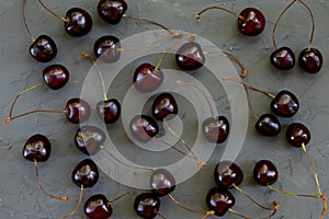 Pattern made of ripe red cherries with stalks lying on dark grey stone textred background. Freshly picked