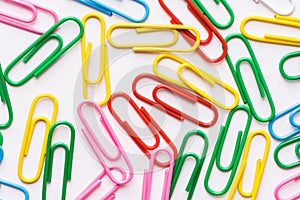Pattern from multicolored paper clips scattered on white background. School office supplies paperwork documents organization