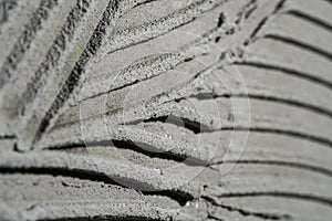 Pattern of notched trowel strokes on the gray surface of cement putty for laying ceramic tiles. Texture of glue paste