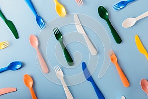 The pattern of reusable cutlery on the blue background. Plastic spoons, forks, knives top view. Summer Picnic. Plastic