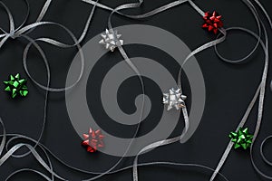 Pattern swirls of silver ribbon and bows for gifts green, red and silver colors. New Year decorations Black background, top view,