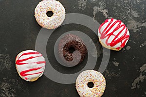 Pattern of various glazed donuts on a black concrete background. Top view, flat lay