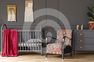 Patterned armchair and grey cabinet next to kid`s bed with red b