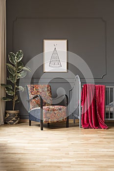Patterned armchair next to bed with red blanket in baby`s bedroo