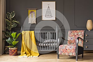 Patterned armchair next to kid`s bed with yellow blanket in bedr