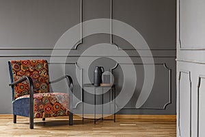 Patterned armchair next to table against grey wall with molding