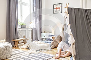 Patterned carpet on parquet of cozy boy`s bedroom with comfortable bed and scandinavian tent, real photo with copy space