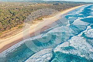 Patterned foamy ocean waves roll in and approach sandy beach. Majesty turquoise sea. Top view drone