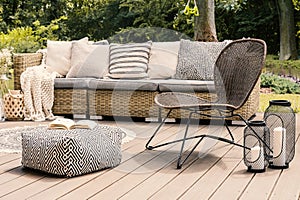 Patterned pouf and rattan chair on wooden patio with pillows on