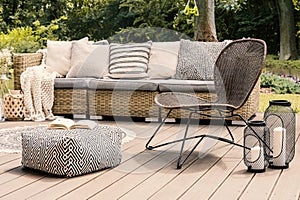 Patterned pouf and rattan chair on wooden patio with pillows on photo