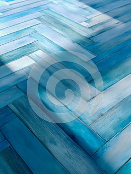 Patterned wooden floor with a herringbone design in various shades of blue illuminated by natural sunlight creating a dynamic and