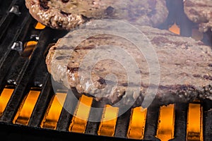 Patties of ground meat on a cooking grate with flames and smoke