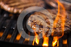 Patties of ground meat with a flame in the front on a cooking gr