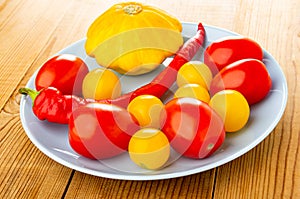 Pattison, chili pepper, red and yellow tomatoes in plate on wooden table