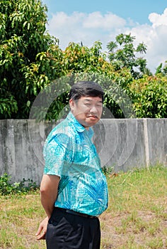 Paunchy senior Asian man standing and smiling in greenfield grass garden