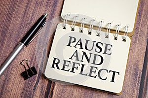 pause and reflect the phrase on white paper and pen on wooden background
