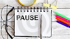 PAUSE written in a notebook on white background with office tools