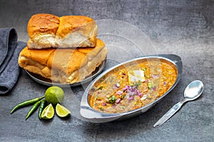 Pav Bhaji is a spicy, buttery mashed vegetable curry served with soft bread rolls, garnished with onions, coriander, and lemon. photo