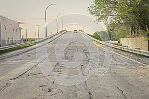 Paved bridge going uphill filled with potholes and surface erosion