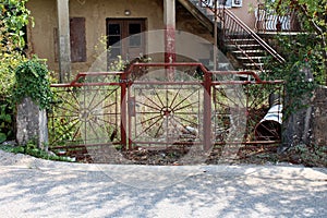 Paved road entrance to abandoned family house blocked with metal doors locked with strong chain leading to overgrown front yard