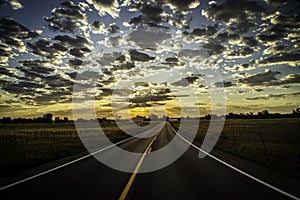 Paved Road leading into the Horizon as sun rays beam out of the clouds