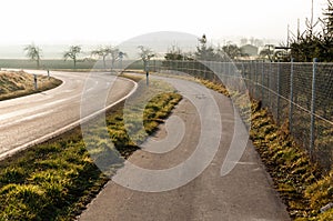 a paved road near an empty highway with grass and bushes in the foreground