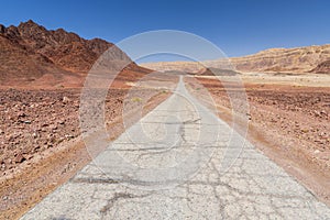 Paved road runs through Arava desert among red mountains in Timna National Park, Israel