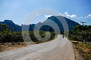 Paved rural road winding through cultivated lands having a forested mountain range in front