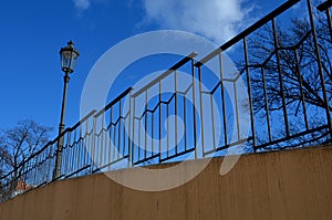 Paved sidewalk with gutter and gray metal ornate railings. lamp with glazed lampshade and black post, by old gas lamps on a city s