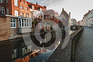 pavement on narrow street and buildings reflected in calm water of canal in brugge, belgium