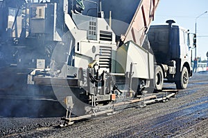 Paver machine laying asphalt, fed by a dump truck