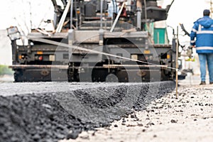 Paver machine is laying fresh asphalt on city road