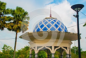 A pavilion with a blue roof and palm trees on sky background. Miri City Fan Park, Borneo, Sarawak, Malaysia