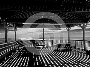 Pavilion with shadows at sunset on beach, waves crashing in distance and dramatic sky