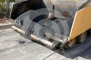 A paving machine placing fresh asphalt or bitumen on a gravel base during