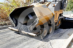 A paving machine placing fresh asphalt or bitumen on a gravel base during