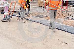 Paving stone workers filling joints of block paved footpath with dry sand during the construction of a new road