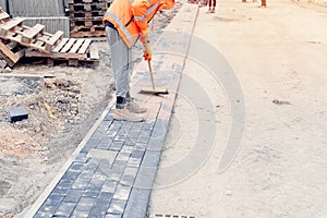 Paving stone workers filling joints of block paved footpath with dry sand during the construction of a new road