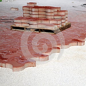 Paving the surface of a square with red concrete blocks of curved shapes.