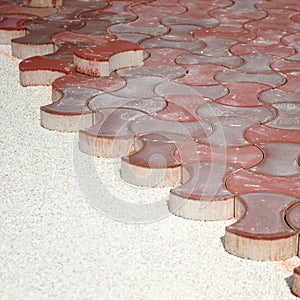 Paving the surface of a square with red concrete blocks of curved shapes.