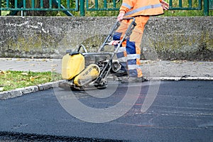 Paving worker uses vibratory plate compactor to compact new asphalt near curbstones