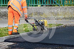 Paving worker uses vibratory plate compactor to compact new asphalt near curbstones
