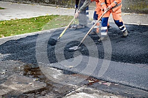 Paving workers move very fast their shovels while adjusting new layer of asphalt in reconstruction of road